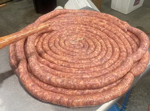 A massive, single continuous coil of fresh, raw pork sausage prepared on a stainless steel commercial kitchen table.