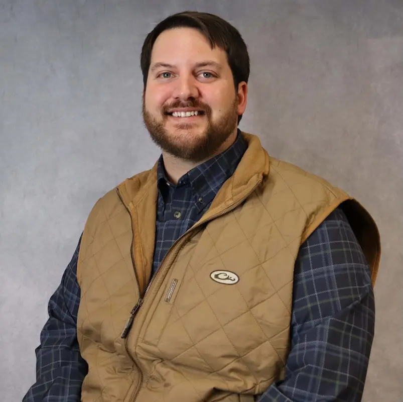 Jake Charpentier: Headshot of Jake Charpentier, Head of Processing at Down The Bayou Meats, wearing a plaid shirt and tan quilted vest.